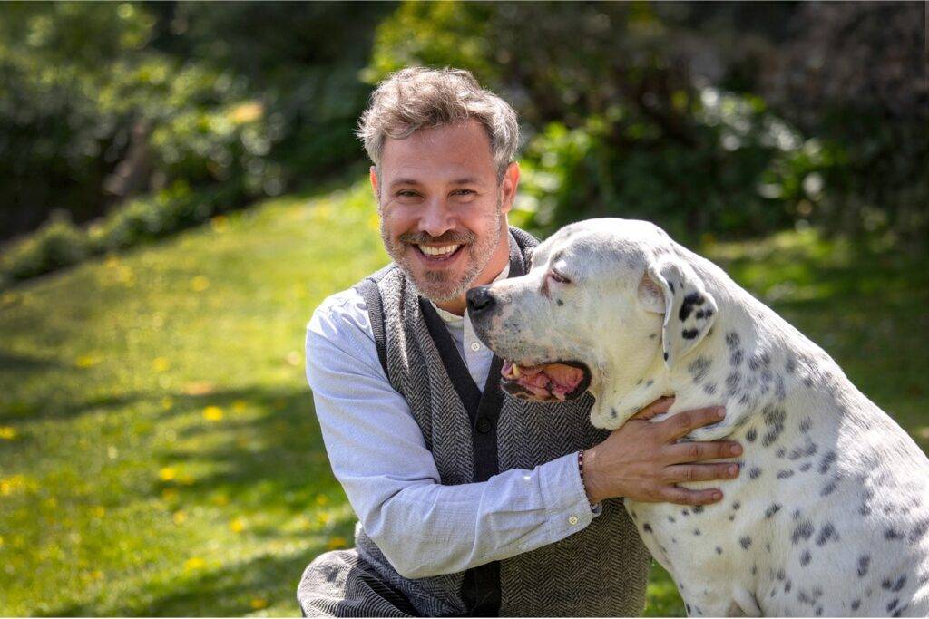 Will Young in a garden petting a black and white spotted dog